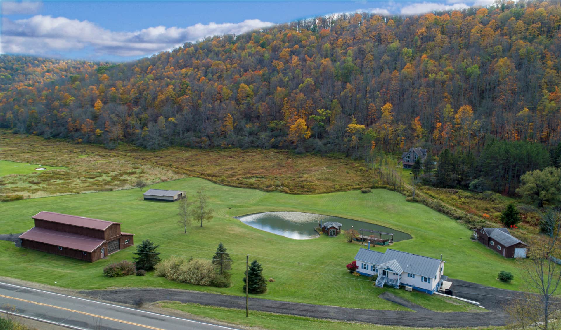 Drone view of The Maples property, pond, lawn, and hills